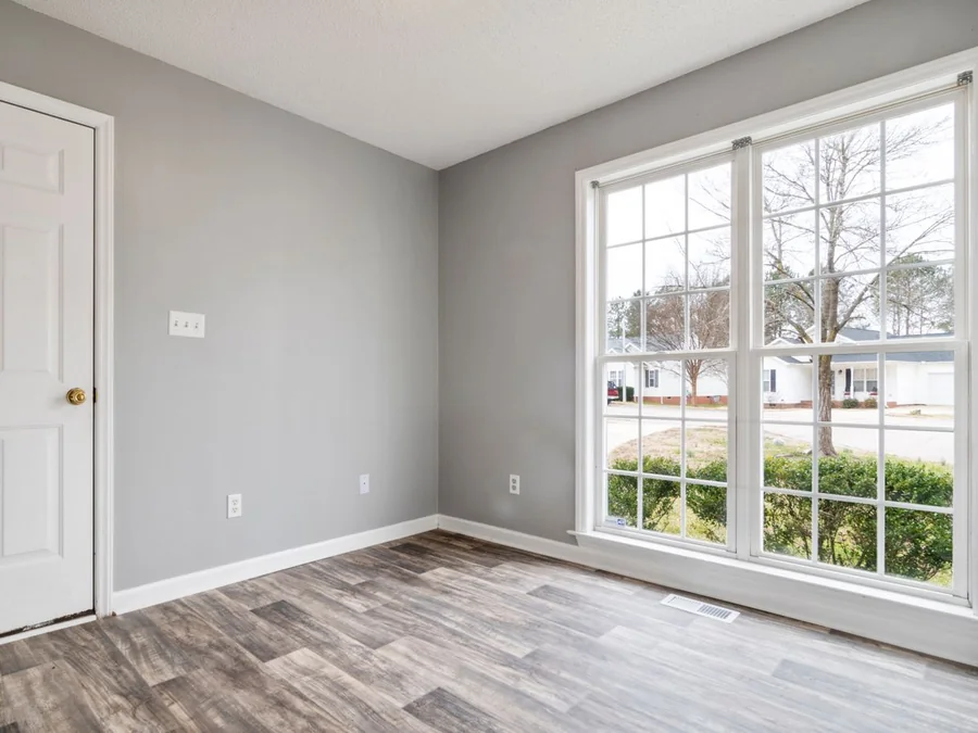 Unfurnished room with pale walls, wood floors and a large sunlit window